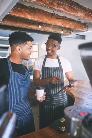 Getting orders out with good old teamwork. two young men using a digital tablet while making coffee at a cafe.の写真素材
