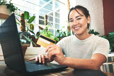 My orders been shipped. Cropped portrait of an attractive young business owner sitting alone in her studio and using a laptop for online shopping.の写真素材