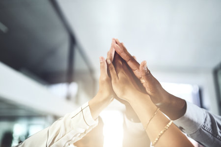 Collaborating to bring success to our teams name. Closeup shot of a group of businesspeople giving each other a high five in an office.の写真素材