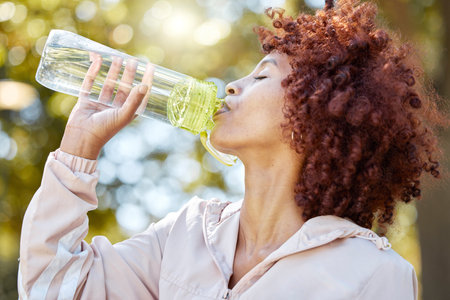 Black woman runner, drinking water and park for summer exercise with curly afro, wellness and...