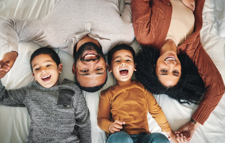 Laughing, family and top view portrait on bed in bedroom, bonding and care in home. Love, smile and happy mother, comic father and funny children playing, having fun and enjoying joke time together.の写真素材