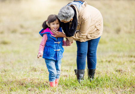 Grandmother, happy girl and nature walk of a kid with senior woman in the countryside. Outdoor field, grass and elderly female with child on a family adventure on vacation with happiness and funの写真素材