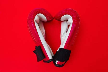 I love boxing. High angle shot of a pair of boxing gloves placed together on top of a red background inside of a studio.の写真素材
