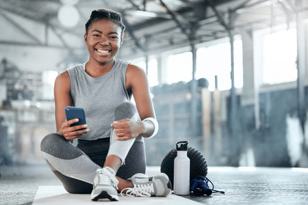 Social media, smile or black woman with phone in gym to search for sports online in training or exercise. Fitness app, happy or healthy athlete relaxing or resting online mobile content on breakの写真素材