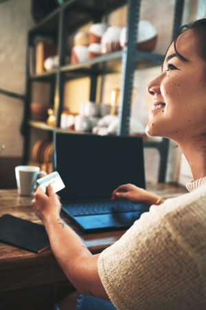 Id buy anything my pottery studio needs. an attractive young business owner sitting alone in her studio and using a laptop for online shopping.の写真素材