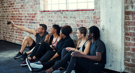 Team photo. a cheerful young group of people sitting down on the floor and taking a self portrait together in a gym.の写真素材