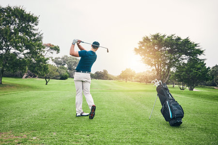 Golf, stroke and training with a sports man swinging a club on a field or course for recreation and fun. Golfing, grass and hobby with a male golfer playing a game on a green during summerの写真素材