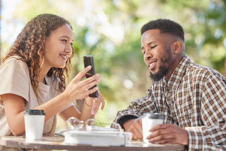 Coffee, black couple and phone outdoor while talking and bonding on date at table. Man and woman at cafe with smartphone and a drink or tea to relax with mobile app, social media or online postの写真素材