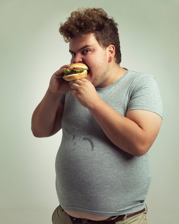 Dont come near my burger. Studio shot of an overweight man biting into a burger.の写真素材