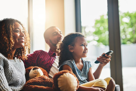 Weekends are about doing what everybody loves. Shot of a happy young family of three watching tv from the sofa at home.の写真素材