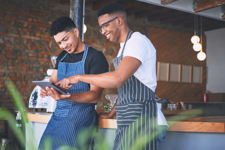 The less paper, the more sustainable. two young men using a digital tablet while working in a cafe.の写真素材