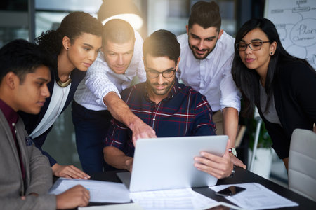 They work seamlessly together. Shot of a group of colleagues working together around a laptop in an office.の写真素材