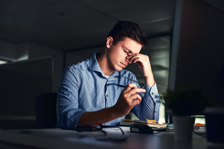 Putting in those overtime hours. Shot of a young businessman working late at night in a modern office.の写真素材