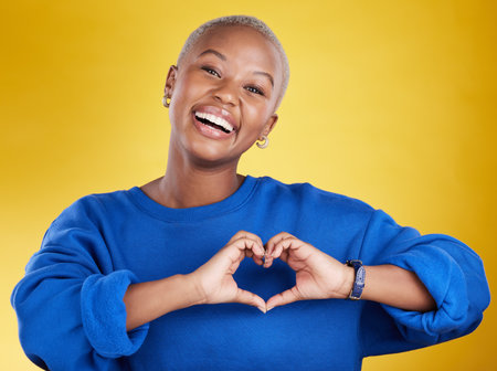 Heart hands, portrait and happy black woman in studio, background and color backdrop for emoji. Smile, female model and finger shape for love, thank you and support of peace, care or sign of kindnessの写真素材