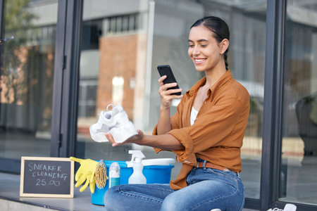 Cleaning woman, phone or shoes service on social media advertising, small business promotion or photograph on city road. Smile, happy or maid on mobile technology for blogging review tips of sneakersの写真素材