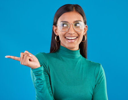 Mockup, Indian woman and pointing with space, smile and advertising with girl against a blue studio background. Female, lady and gesture for direction, happiness and branding development with smileの写真素材
