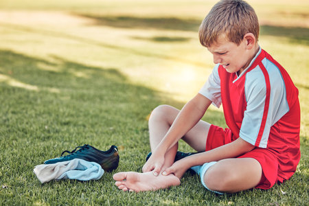 Soccer, injury and pain of child foot on field cry for medical emergency, healthcare insurance and wellness. Football, soccer field and sad kid crying with legs massage for sports training accidentの写真素材