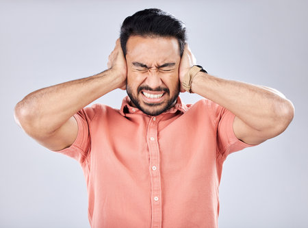 Loud, mental health and angry Asian man with schizophrenia isolated on a grey studio background. Stress, fear and scared guy closing ears for noise, scared and bipolar pressure on a backdropの写真素材