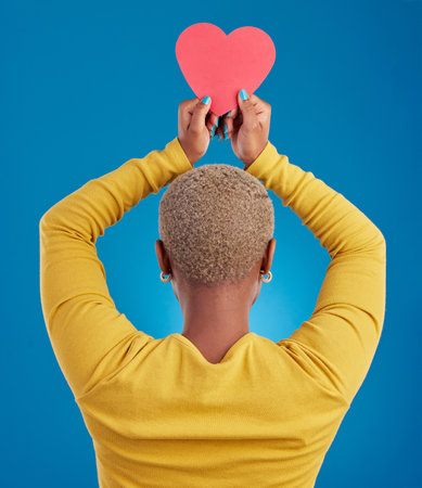 Paper, heart and back of black woman in studio for love, date and kindness. Invitation, romance and feelings with female and shape isolated on blue background for emotion, support and affectionateの写真素材