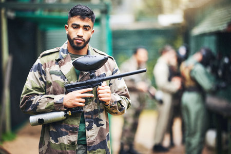 Paintball game and portrait of a man with gun and safety uniform for outdoor shooting battle. Assertive and young indian guy in camouflage clothing ready for shooter sport and activity.の写真素材