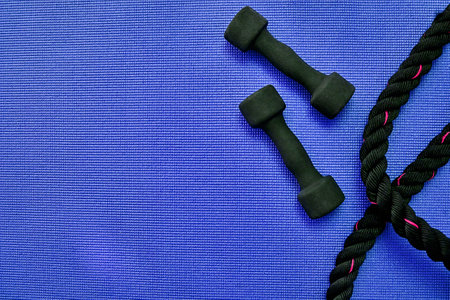 Whos ready for a workout. High angle shot of two lightweight dumbbells and piece of rope placed on a blue background inside of a studio.の写真素材