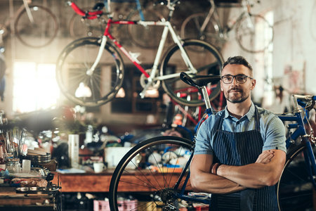 Portrait, serious and repair man in bicycle shop with arms crossed working in workshop. Face, bike mechanic and confident male person, professional or mature technician with glasses in small businessの写真素材