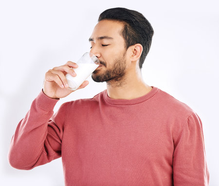 Man drinking glass of milk in studio, white background and backdrop for healthy dairy, smoothies and diet. Male model, cup and calcium of smoothie, vanilla milkshake and nutrition of protein drinkの写真素材