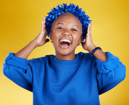 Portrait, queen and flower crown with an excited black woman in studio on a yellow background. Face, expression and sustainability with an attractive female wearing a blue wreath as royaltyの写真素材