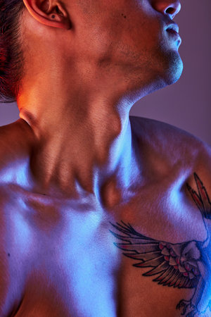 Man, chest and neon light in studio for art, fitness or beauty of a person on a gray background. Strong body, neck and male model with a tattoo, glow and creative motivation for aesthetic backdropの写真素材