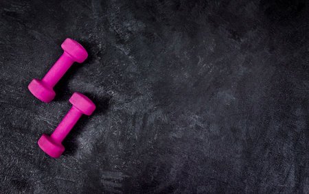 Were pretty light weight. High angle shot of two lightweight dumbbells placed on a dark background inside of a studio.の写真素材