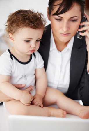 Woman, home office and phone call with baby, laptop or care with talk, reading or multitasking at desk. Mother, young boy child and cellphone for networking, bond or remote work at pc in family houseの写真素材