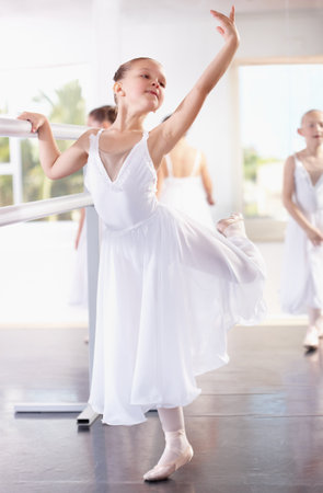 Girl ballerina pose at barre, ballet and dance class with young dancer learning balance and art at studio. Female child in lesson at academy, creativity with fitness and training, elegance and focusの写真素材