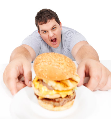 Plus size, portrait of man holding burger and unhealthy diet, isolated hungry person and white background. Junk food, weight loss and healthcare problem, cholesterol or fat food addiction in studio.の写真素材