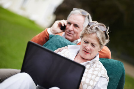 Phone call, laptop and travel with an old couple in a hotel garden for vacation at a luxury resort. Love, technology or communication with a senior man and woman tourist outdoor on grass at a lodgeの写真素材