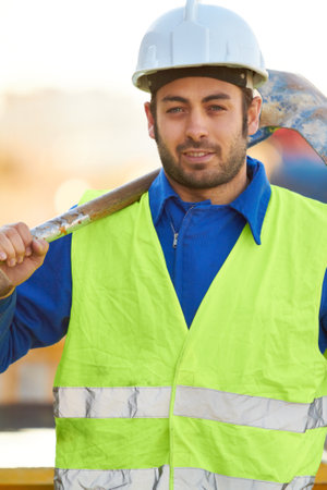 Portrait, construction and man with a shovel, industry and architecture with skills, renovation and vest. Face, male person or employee with tools, equipment or safety with labor, spade or protectionの写真素材