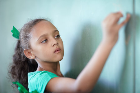 Education, focus and a girl writing on a chalkboard for learning, studying and teaching in class. Creative, concentration and a young student at a blackboard for a presentation or classroom notesの写真素材