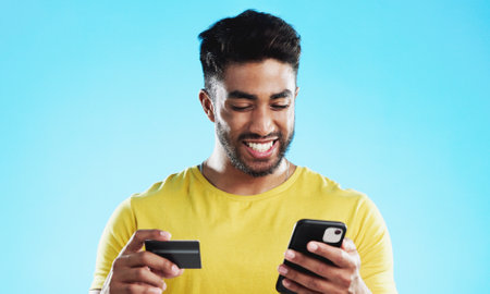 Online shopping, excited or happy man with credit card, phone or digital bank payment for studio fintech sale. Finance app, e commerce banking trade or customer search retail product on store websiteの写真素材