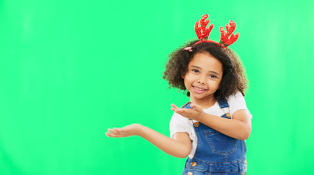 Christmas, green screen and a girl presenting advertising space for product placement in studio. Portrait, kids or celebration with an adorable little child on chromakey mockup for the festive seasonの写真素材