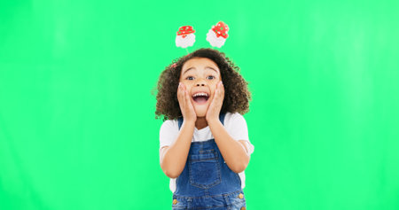Excited, happy face and child with green screen and smile and Christmas headband ready for celebration. Comic, surprised and shocked portrait of a young girl with happiness about holiday eventの写真素材