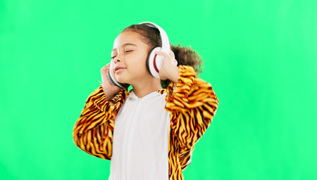 Children, music and dance with a girl on a green screen background in studio streaming audio while having fun. Kids, energy and freedom with a little female child dancing while listening to the radioの写真素材