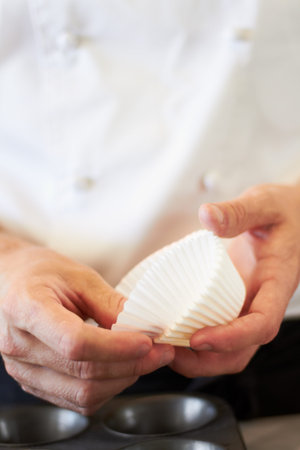 Cupcake, person hands and baking in a kitchen with muffin wrapper and cooking in a bakery. Prepare,...
