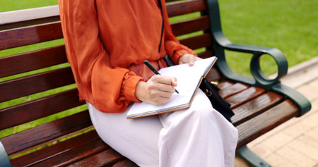 Park, bench and a woman writing in a notebook, diary or journal while outdoor in a garden to relax....