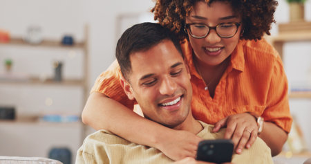Love, social media and happy couple on sofa with phone, happiness and checking meme in apartment. Smile, man and woman on couch in living room, smartphone and quality time bonding together in home.の写真素材