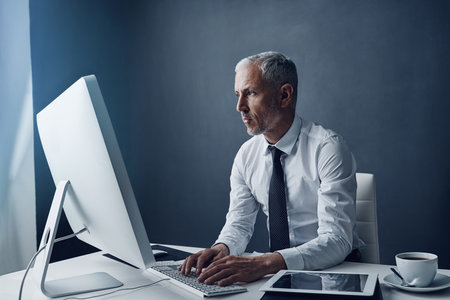 Computer, typing accountant and senior man in office, working on project online or mockup. Desktop, writing and serious manager at desk for reading email, research information or business auditor.の写真素材