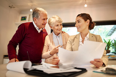 Senior couple, financial advisor and paperwork in discussion for budget or retirement plan at home. Happy elderly man and woman with consultant or lawyer and documents for investment planning or loanの写真素材
