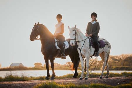 Horse riding, sunset and hobby with friends in nature on horseback by the lake during a summer morning. Countryside, equestrian and female riders outdoor together for travel, hobby or adventureの写真素材