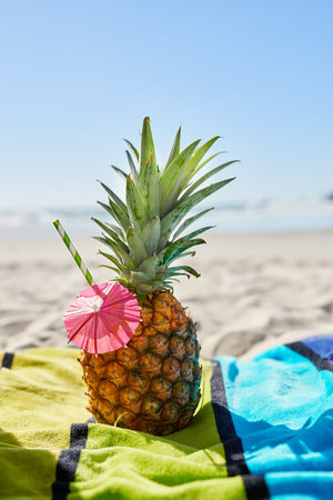 Cocktail, travel and closeup of a pineapple on a beach with alcohol on a towel for vacation. Summer,...