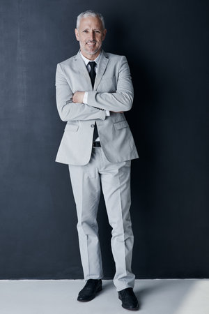 Studio portrait of mature man in suit, arms crossed and smile on dark background. Confidence, pride and professional career for happy executive businessman or senior business owner or successful ceo.の写真素材