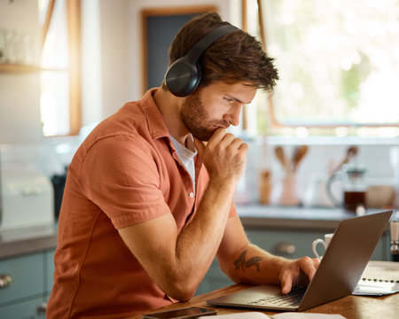 Thinking, home kitchen and man focus on laptop data, streaming music or reading web info, news or blog. Brainstorming idea, planning or person listening to audio podcast and working remote on projectの写真素材