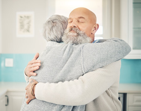 Love, romance and senior couple hugging in the kitchen together in their modern house. Happy, sweet and elderly man embracing his wife with care, affection and happiness for bonding in their home.の写真素材